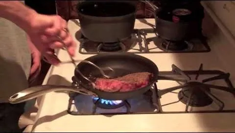 Cooking steak in a skillet on a gas stove.