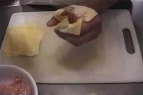 Hand holding a piece of dough on a cutting board.