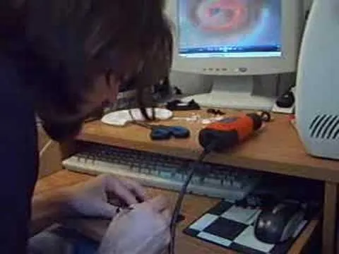 A person working on a computer repair at a desk with tools and a monitor in the background.