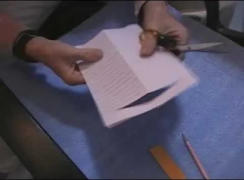 Person cutting paper with scissors on a blue surface.