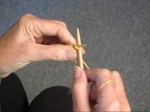 Hands demonstrating a knitting technique with two wooden needles and yarn.