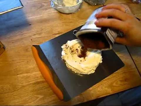 Person pouring cocoa powder onto a cake with icing.