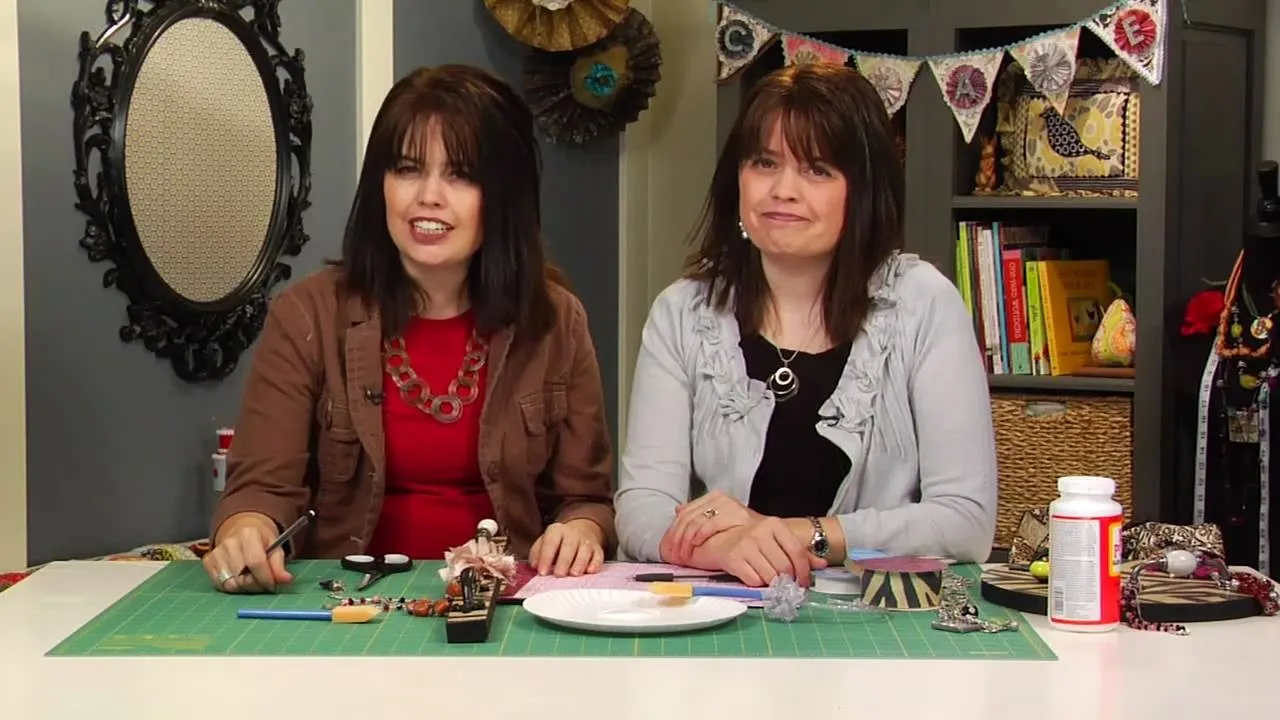 Two women smiling at a crafting table with various supplies.