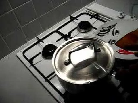 A hand holding a lid over a pot on a gas stove.