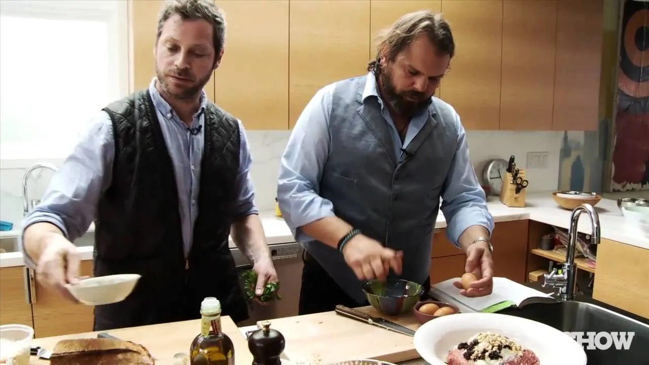 Two men cooking in a modern kitchen, with one preparing ingredients and the other mixing a dish.