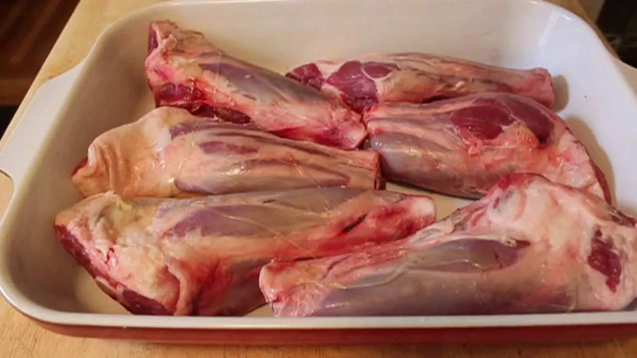 Raw lamb shanks arranged in a white baking dish.