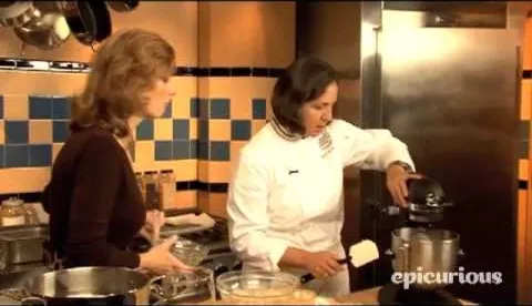 Two women cooking in a professional kitchen, one using a stand mixer.
