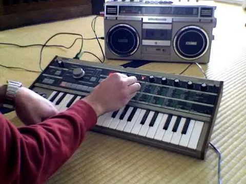 Person playing a vintage synthesizer in front of a boombox.