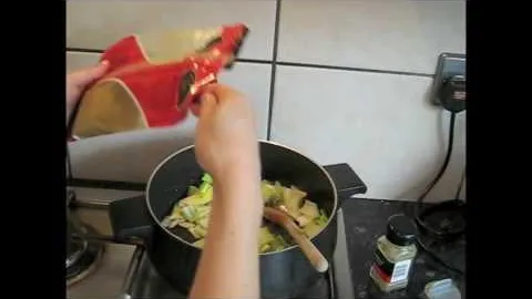 Person adding ingredients from a red packet into a pot on the stove.