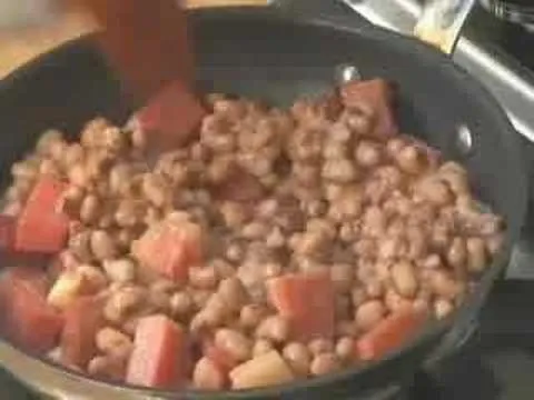 Pinto beans cooking in a skillet with diced vegetables.