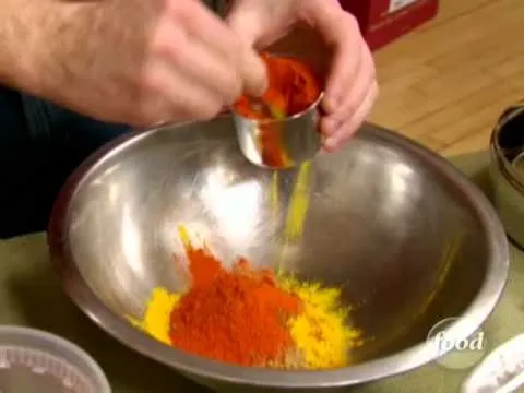 Measuring and mixing spices in a metal bowl.
