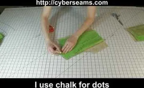 Person using chalk on green fabric for crafting or sewing on a grid cutting mat.