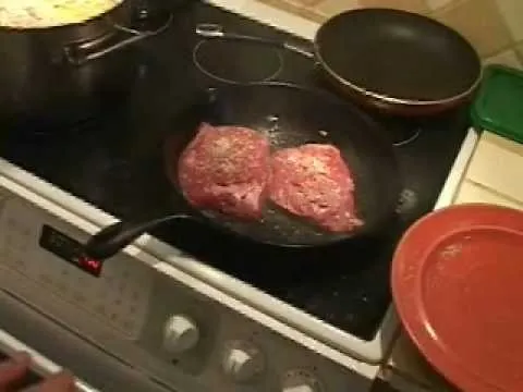 Cooking meat in a frying pan on a stovetop.