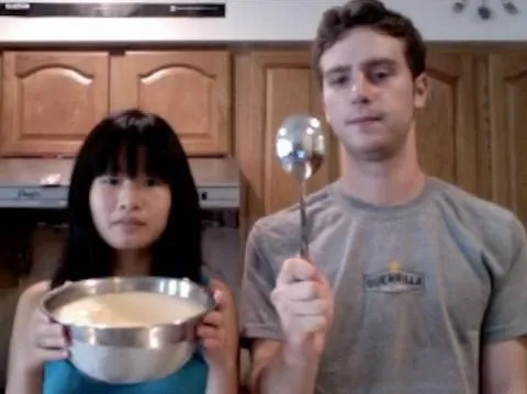 Two individuals in a kitchen, one holding a bowl and the other holding a ladle.