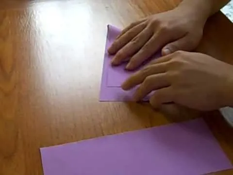 Hands folding a purple piece of paper on a wooden surface.