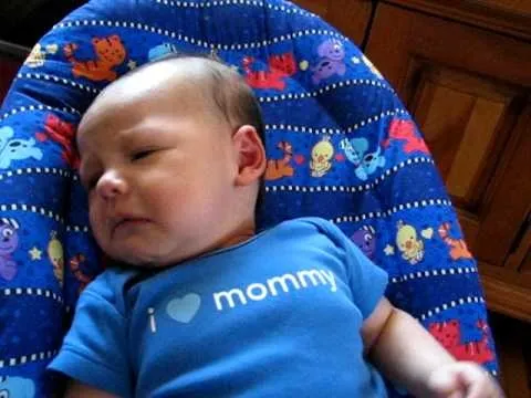 Baby in a blue onesie with "I love mommy" text, resting in a decorated bouncer.