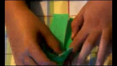 Hands folding green paper on a colorful surface.