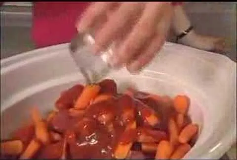 Hand pouring sauce over a dish of carrots and meat.