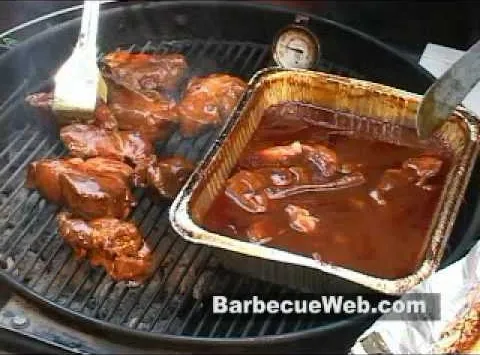 Grilled meat and barbecue sauce in a tray on a barbecue grill.
