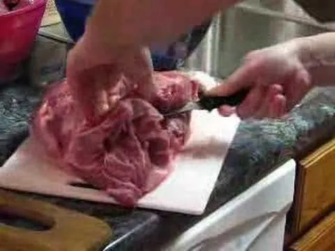Slicing raw meat on a cutting board in a kitchen.