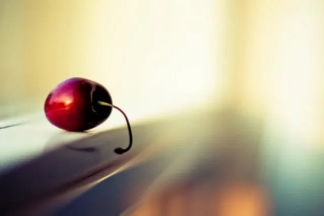 A single cherry on a reflective surface.