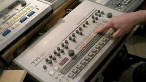 Roland TR-808 drum machine with a finger pointing at controls.