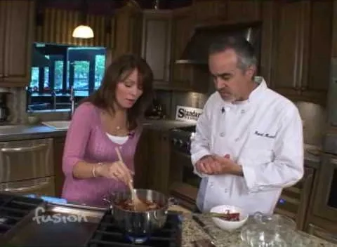 A chef demonstrates cooking techniques with a woman in a kitchen setting.