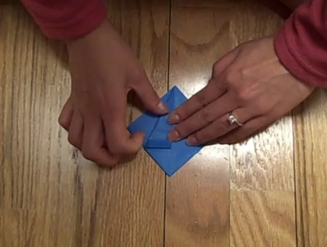 Hands folding a blue origami paper on a wooden surface.