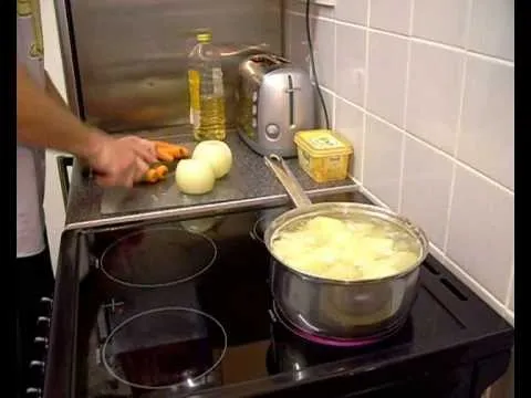 Chopping vegetables near a pot of boiling potatoes in a kitchen.