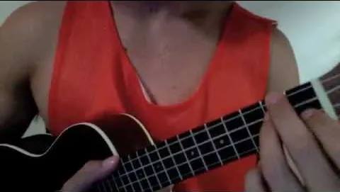 Person playing a ukulele while wearing an orange tank top.