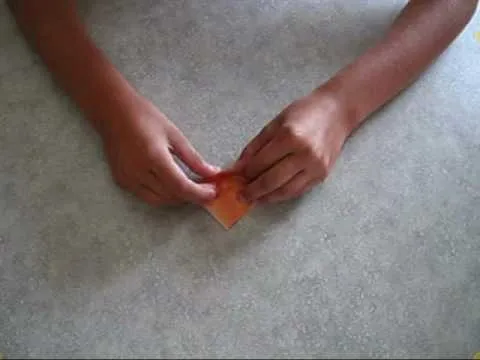 Hands folding a piece of orange paper on a table.