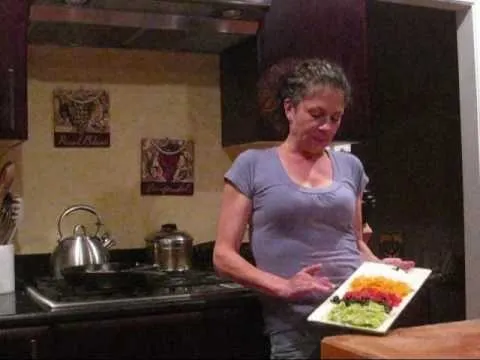 Woman holding a colorful vegetable platter in a kitchen.