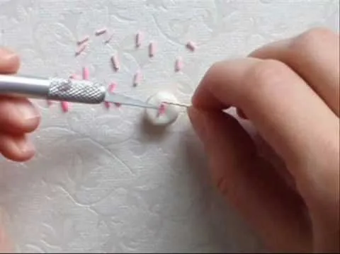 A person using a tool to create decorative designs on a surface with small pink pieces nearby.