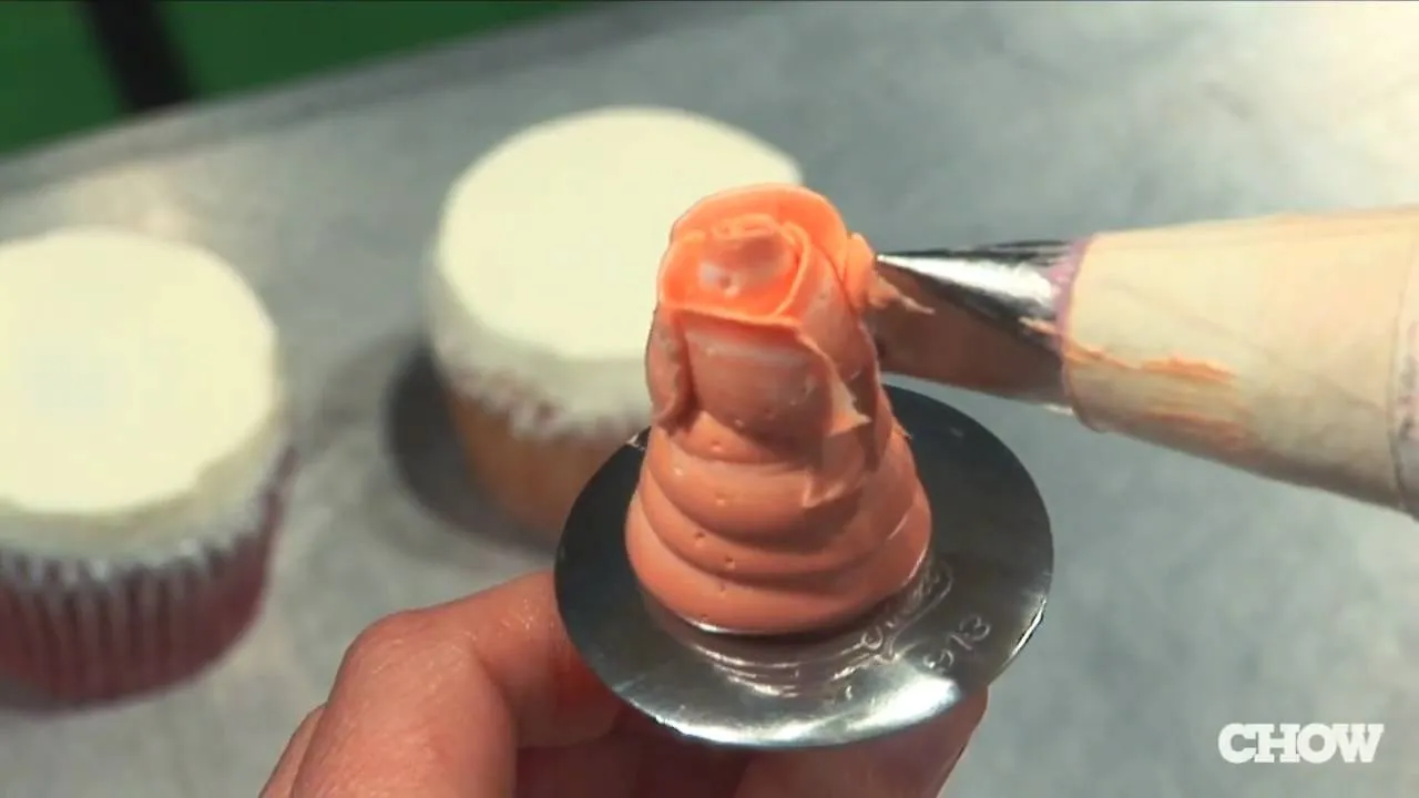 Piping peach frosting onto a cupcake.