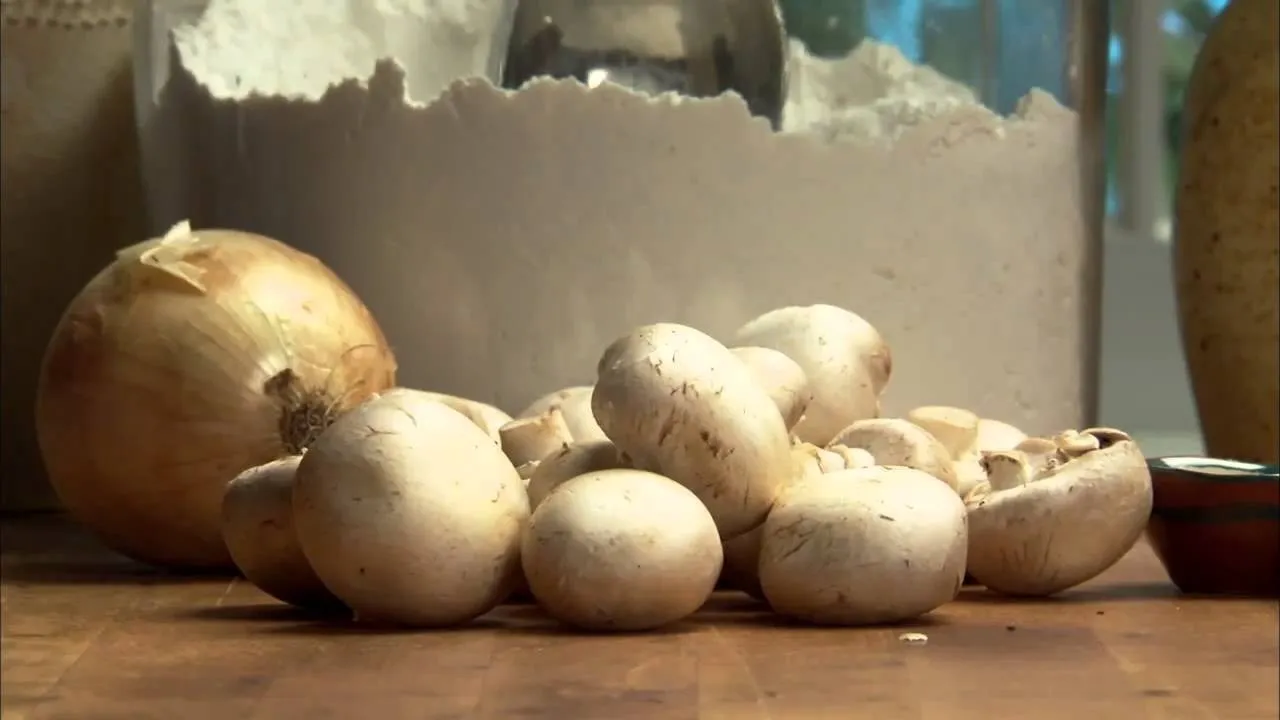 Fresh white mushrooms and an onion on a wooden countertop.