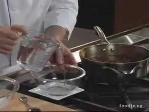 A chef pouring water into a measuring cup above a bowl and a pan on a stovetop.