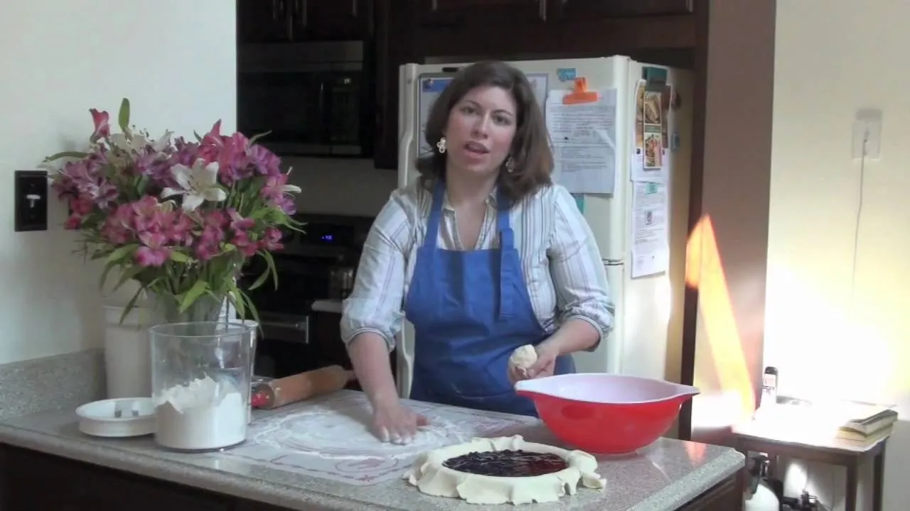 Woman preparing dough in a kitchen with flowers and ingredients on the counter.