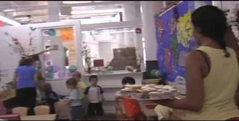 Children engaged in an art classroom activity with a teacher serving snacks.