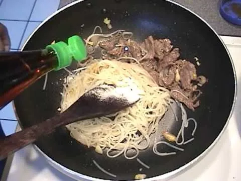 Stir-fried noodles with beef and vegetables in a frying pan.