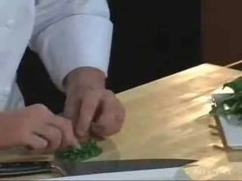 Chef chopping herbs on a wooden countertop.