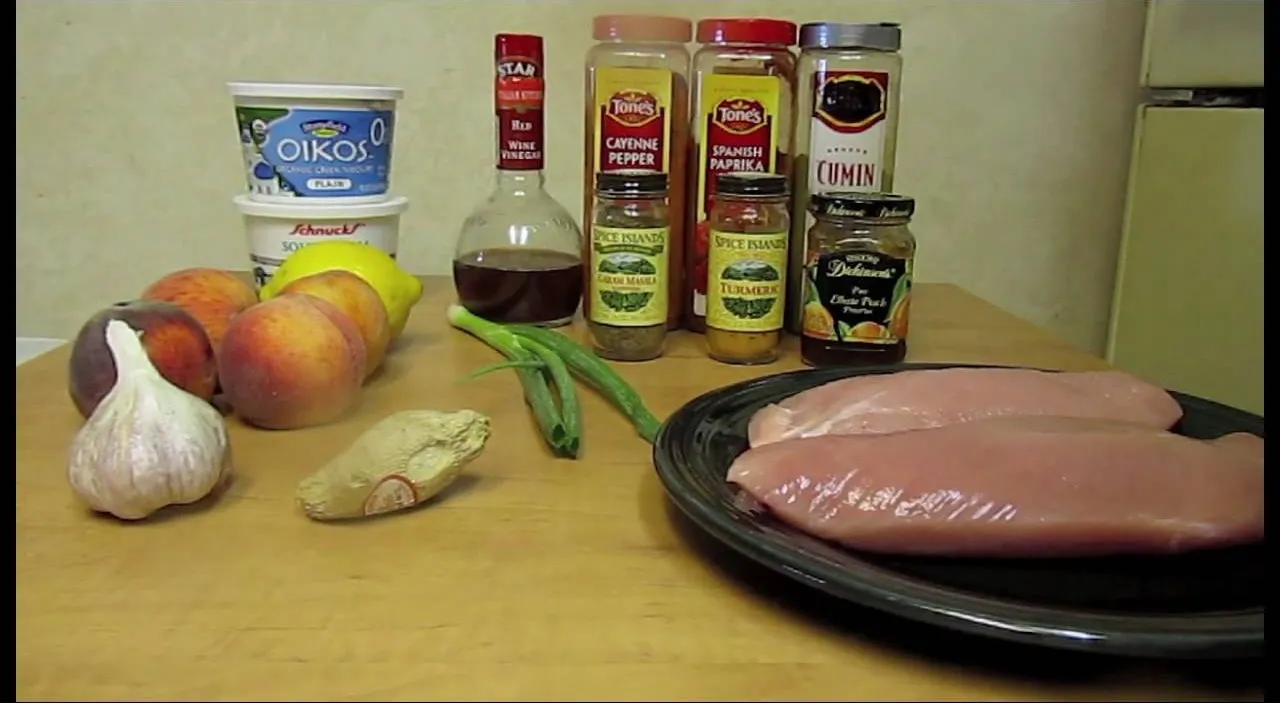 Ingredients for a chicken dish, including chicken breasts, spices, garlic, peaches, and yogurt.