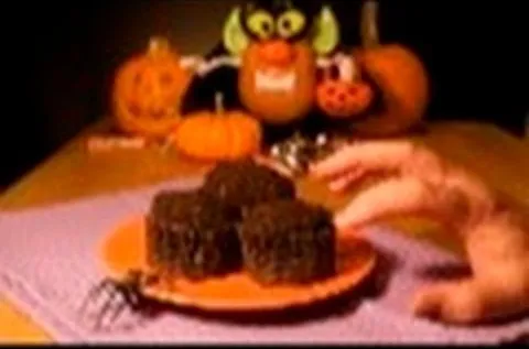 Chocolate cupcakes decorated for Halloween with a hand reaching for one and pumpkins in the background.