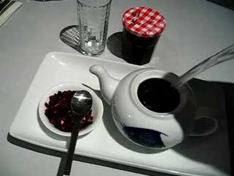 Tea pot with a glass of water, a bowl of dried fruit, and a jar of jam on a white plate.