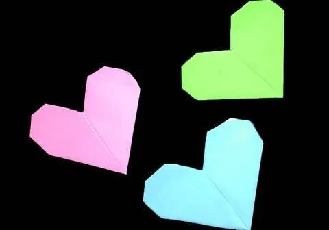 Three colorful origami hearts in pink, green, and blue on a black background.