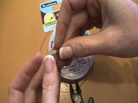 Hand holding a piece of jewelry-making wire with tools and supplies in the background.