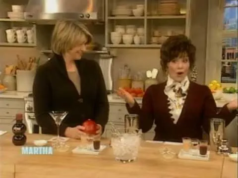 Two women in a kitchen setting, one presenting a beverage and the other smiling.