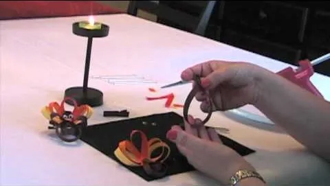 A person crafting a decorative item using colored ribbons and a small candle on a table.
