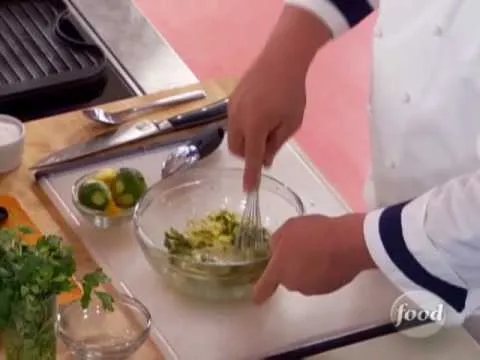 Chef preparing a green sauce in a glass bowl.