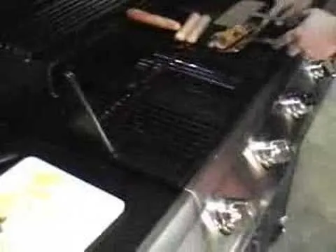 Grill with hot dogs and cooking utensils.