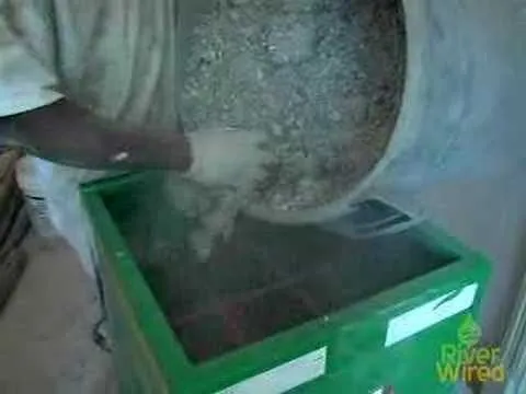 A worker pouring materials into a green recycling bin.